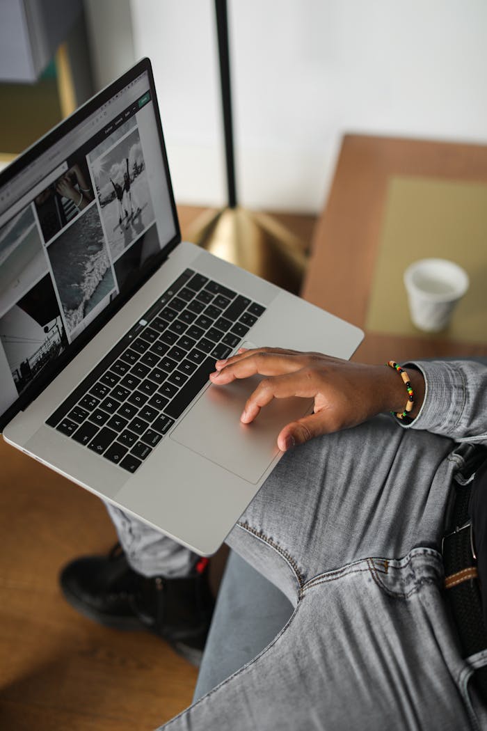 Person uses laptop indoors, viewing photos, wearing denim pants in a relaxed setting.